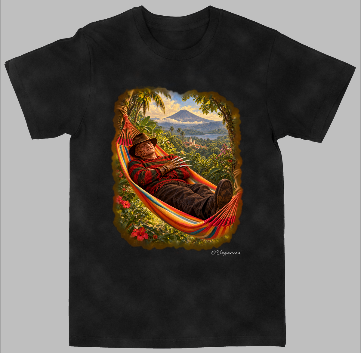 A black short-sleeve crewneck t-shirt featuring a large, colorful graphic print on the front. The graphic depicts  Freddy Krueger relaxing in a striped red, orange, and yellow hammock surrounded by lush tropical foliage, with a scenic mountain landscape in the background.